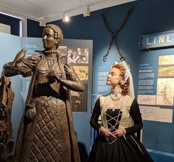 An actress playing Mary Queen of Scots standing next to a statue of the queen